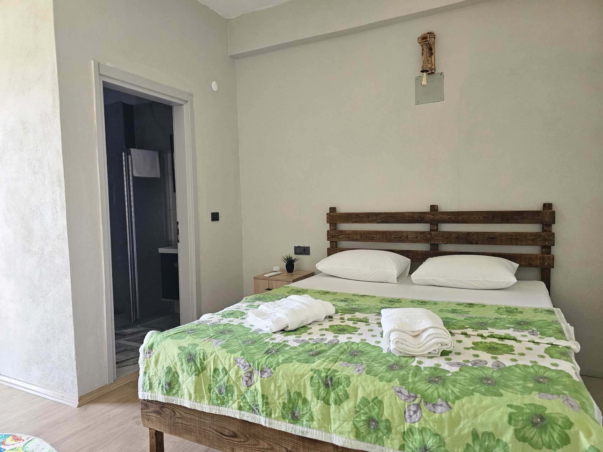 Standart oda; ahşap başlıklı çift kişilik yatak ve banyo girişi
